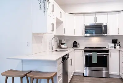 a white kitchen with a counter and two stools at Powder Village Retreat by Revelstoke Vacations in Revelstoke