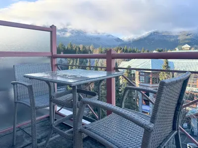 a table and chairs on a balcony with mountains at Alpenglow Lodge Rainbow Look Out Studio by MVA in Whistler