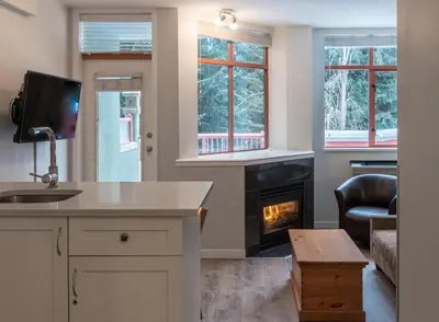 a kitchen with a living room with a fireplace at Alpenglow Lodge Family Studio with Murphy Bed by MVA in Whistler