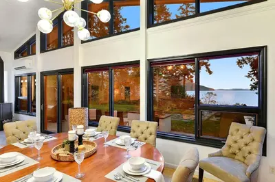 a dining room with a table and chairs and large windows at Beachside Living Cherry Point by EMR Vacation Rentals in Cobble Hill