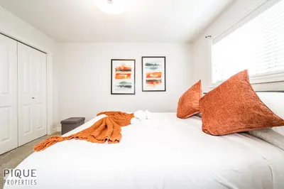 a white bedroom with a large bed with orange pillows at LUXURIOUS 6 Bed Home I Fireplace I near Sports Park I with Double Garage & Fast WiFi! in Edmonton