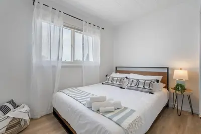 a white bedroom with a large bed with a window at The Hidden Loft I 5-min Walk 2 Beach I DT I 55 TV in Sylvan Lake