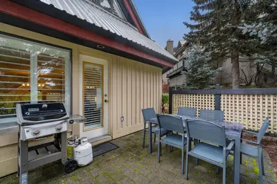 a patio with a grill and chairs and a table with a barbecue at 2BR in Snowberry, Wood Burning Fireplace, Modern Finishes, Parking, Ski Hill Shuttle in Whistler