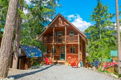a log home with a deck and red chairs at Whiskey Jack, 4 Bedroom Cabin with Outdoor Firepit in Sunshine Valley