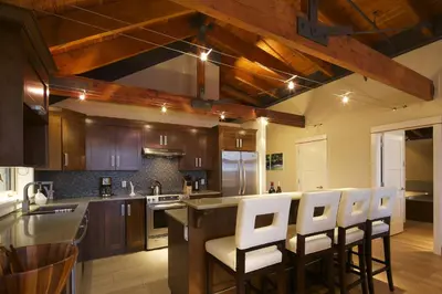 a kitchen with wooden cabinets and a bar with white chairs at Mariner's Loft - Salt Spring Island in Ganges