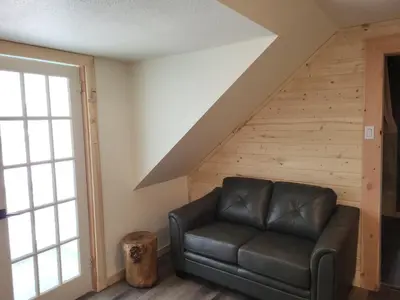 a living room with a leather couch and a staircase at THE ORCHARD (HOSTEL WITH PRIVATE BUNKS) in Radium Hot Springs