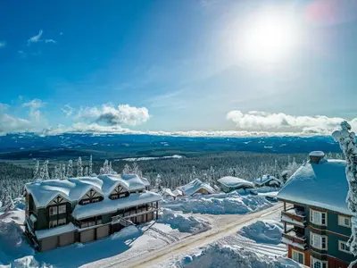 a building covered in snow with the sun in the background at Grizzly Ridge Getaway - Private Hot Tub, Mtn View & Sleeps 11 in Big White