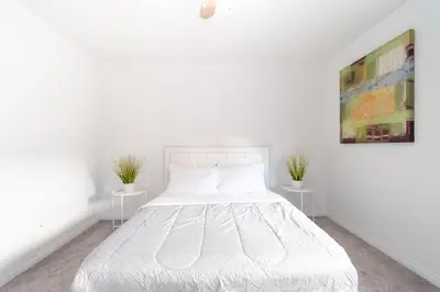 a white bed in a white bedroom with two tables at Spacious & Modern by the Beach in White Rock