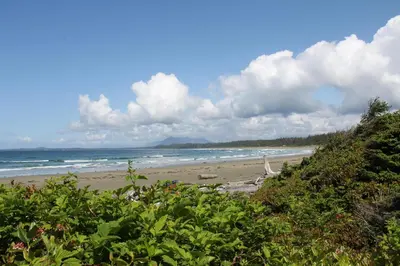 a beach with the ocean and clouds in the sky at Salt Loft - Oceanfront, Hot Tub And Firepit! in Ucluelet