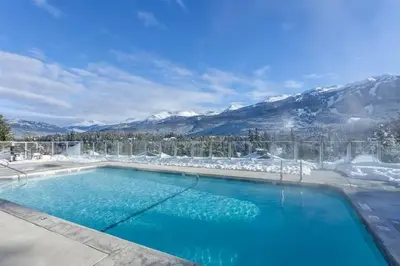 a swimming pool with snow covered mountains in the background at Ironwoods on Blueberry Hill by Whistler Blackcomb Vacation Rentals in Whistler
