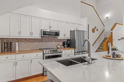 a kitchen with white cabinets and a stainless steel sink at Attractive Downtown Condo! Hot Tub, Mountain Views managed by Little Sister Getaways in Canmore