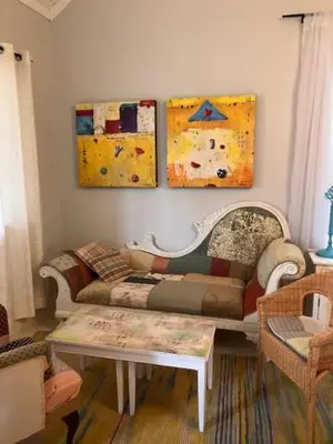 a living room with a couch and paintings on the wall at Cozy ,artistic cottage in a garden setting close to the beach and hiking trails. in Powell River