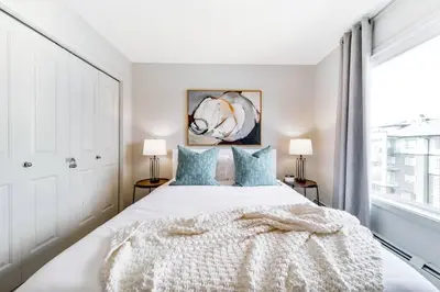 a white bedroom with a large bed with blue pillows at Bright Luxe Condo, AC, Top Floor, King Bed, Balcony! in Edmonton