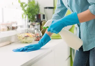 a woman in blue gloves cleaning a counter with a brush at Peaceful Oasis Condo, AC, Top Floor, Secure UG Parking, Balcony, King Bed! in Edmonton