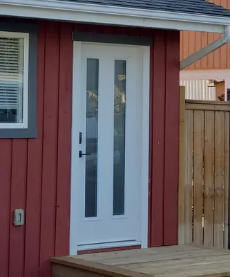 a white door on a red house with a wooden porch at Global Village Permaculture BnB in Oliver