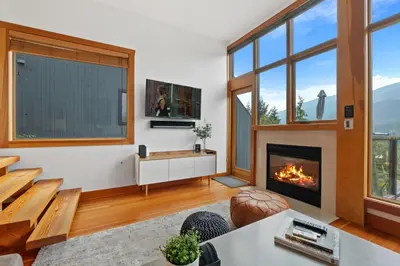 a living room with a fireplace and windows at Whistler 'Treehouse' in Whistler