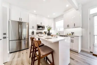a kitchen with white cabinets and a kitchen island with chairs at Modern Nordic Escape, 3BR Near WEM & DT, AirCon & Fireplace, Wifi, Sleeps 6! in Edmonton