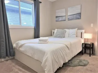 a white bed in a bedroom with a window at Stylish Getaway by Spruce Meadows in Calgary
