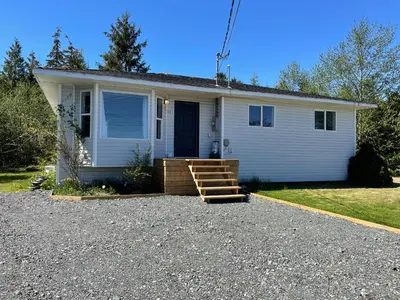 a small white house with a porch and a staircase at Sunrise Mountain view Skidegate House in Skidegate
