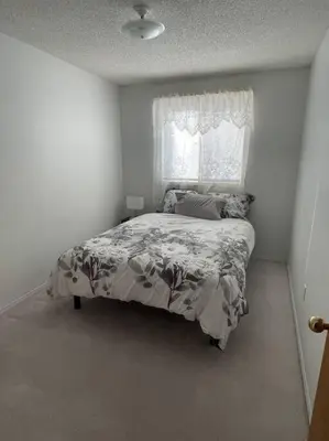 a white bedroom with a bed with a window at Cozy Home in Camrose