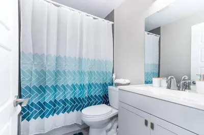 a bathroom with a white toilet and a blue and white shower curtain at Modern & Stylish 2-Bedroom Unit in Edmonton