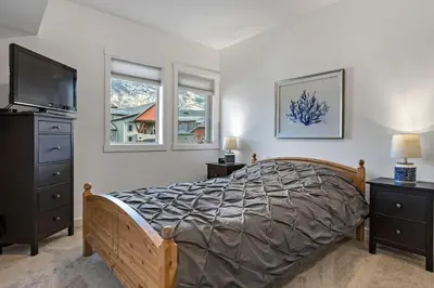 a bedroom with a bed and a tv and two windows at Mountain Retreat - Modern and Bright with Panorama Views 2 bedrooms, 4 beds, heated all-year outdoor pool, hottub, balcony, Banff Park Pass in Canmore