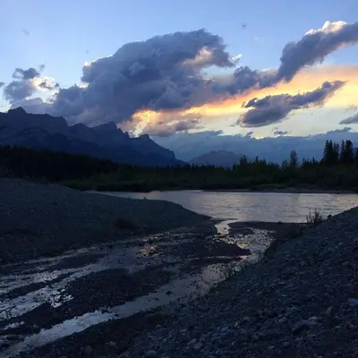 a sunset over a river with mountains in the background at Wanna get away next Summer and Fall at the Crossing in Canmore