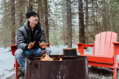 a man sitting in front of a fire at Sundance By Basecamp in Kananaskis Village
