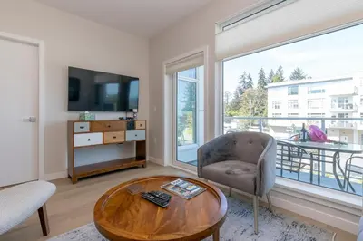 a living room with a table and a chair and a television at Live The Dream In The Haro in Saanichton