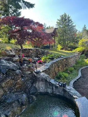 a pond in a garden with a stone wall at Shambhala Zen Suite in Nanoose Bay