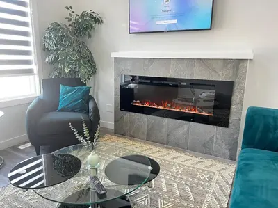 a living room with a fireplace and a chair and a table at Gorgeous 6BR New Home for Families in Nisku