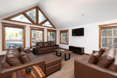 a living room with brown leather furniture and windows at The Evergreen Cabin in Valemount